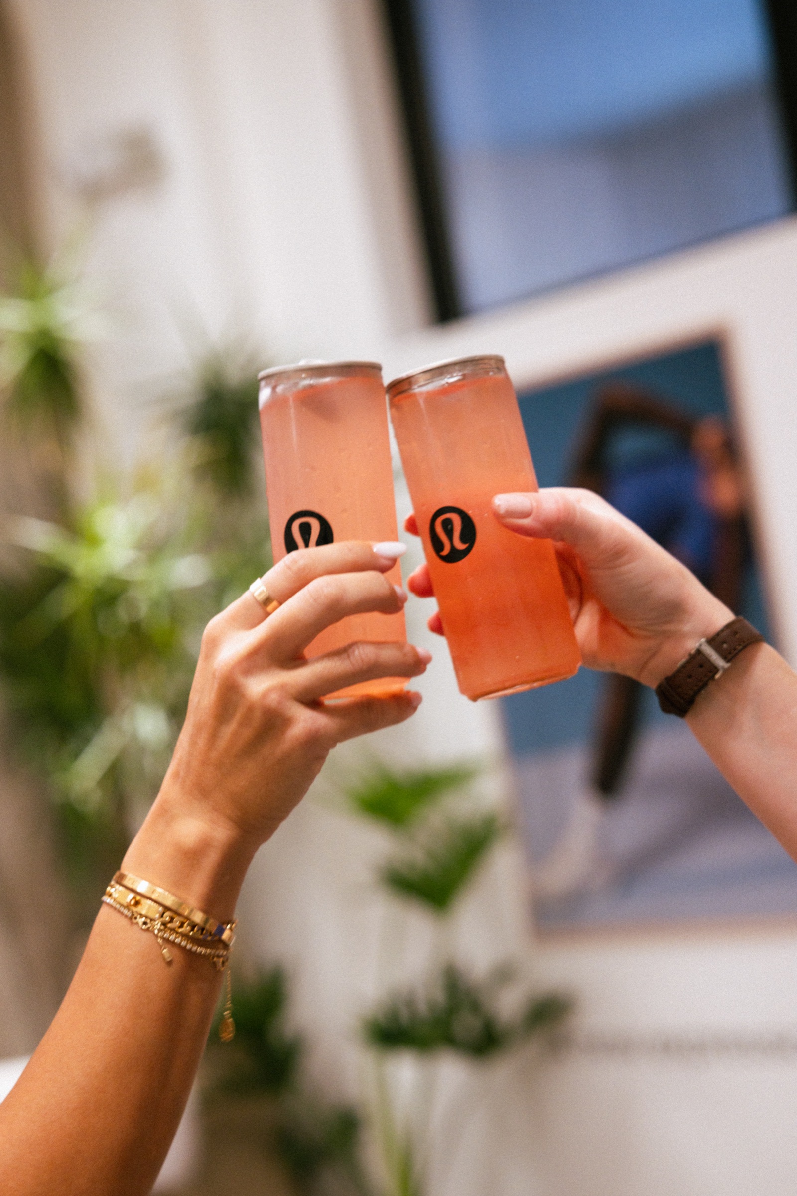 Guests toasting with branded transparent cans of a pink watermelon drink at a private Pilates event